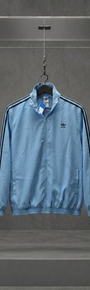 Jaqueta Adidas Originals Fifty-One azul-clara com três listras escuras nas mangas, em vitrine de acrílico